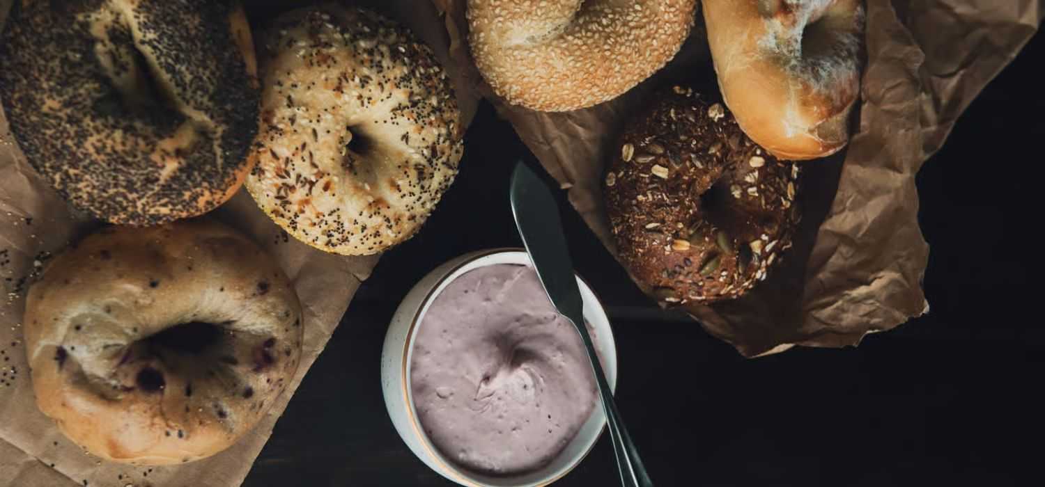 Assorted bagels with cream cheese spread on a dark table.