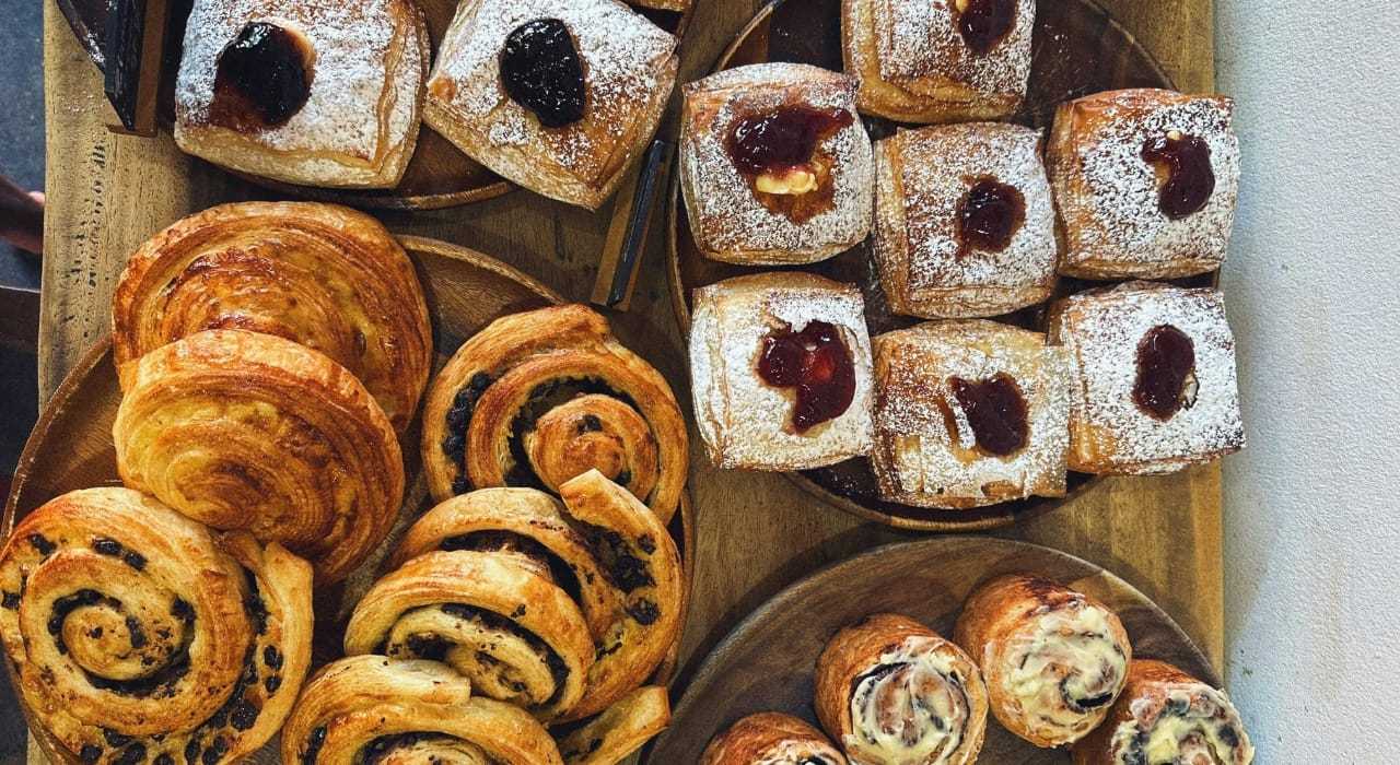 Assorted pastries including croissants and jam-filled pastries on a wooden tray.