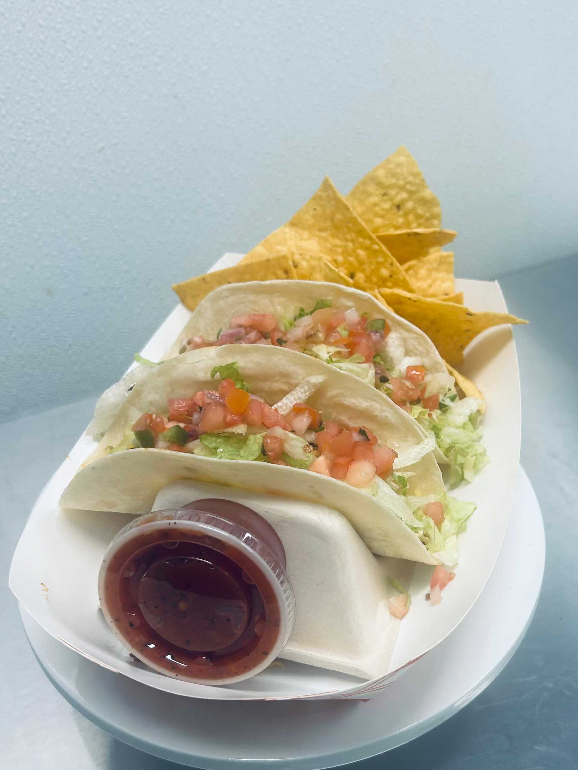 Tacos with salsa, topped with lettuce and tomato, served with tortilla chips.